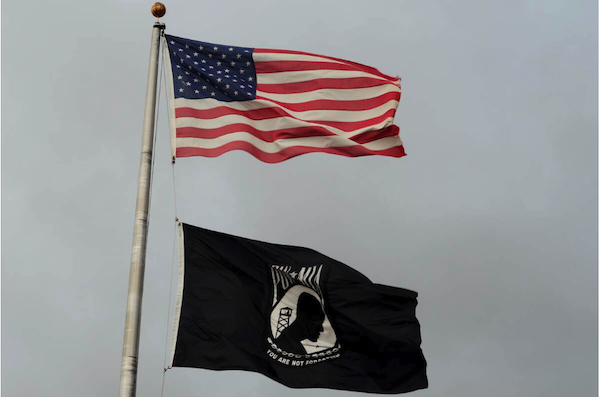 Photo of American flag flying over black and white POW/MIA flag.